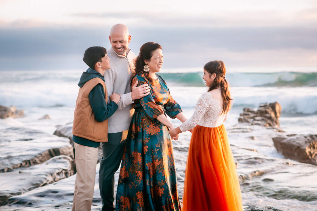 Mother, father, son, and daughter looking at each other while standing on a rock at Windansea Beach